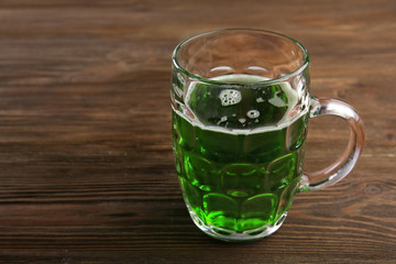 Glass of green beer on wooden background