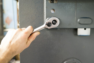 Man tighten screw by socket wrench on industrial equipment