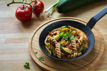 Vegetables with whole grain pasta in a rustic pan on a wooden kitchen board