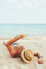 Fototapeta na wymiar Handsome man reading book at the white sand beach