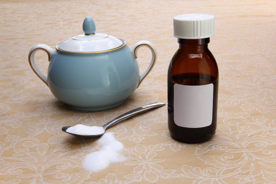 Medicine bottle with plain white label, sugar bowl, and a teaspoon of sugar