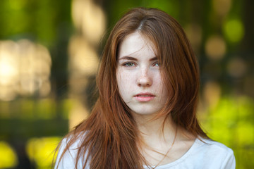 Portrait of a young redhead woman staring into the camera outdoor blurry forest park background