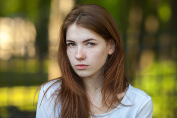 Naklejka premium Portrait of a serious young redhead woman outdoor blurry forest park background