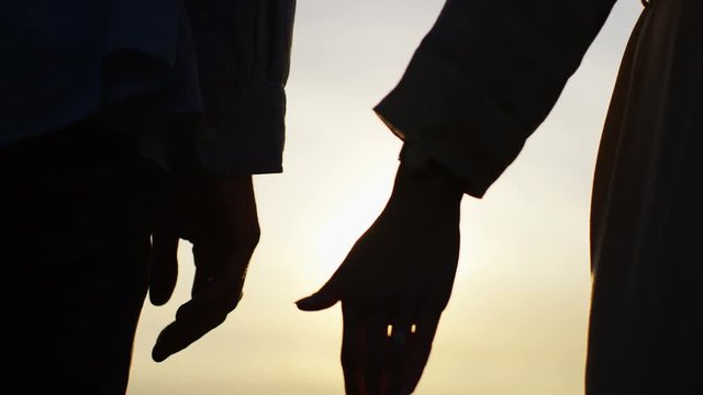 4K Silhouette hands of a couple come together at sunset