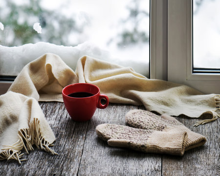 Red cup of coffee or tea, beige scarf and womans mittens.