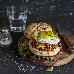 Homemade burger with fried egg and coleslaw on rustic wooden board on a dark stone background. Healthy delicious food