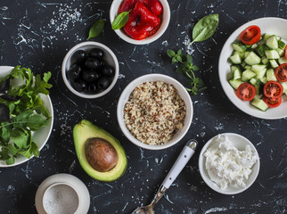 Quinoa, avocado, roasted peppers, fresh cucumbers and tomatoes, arugula, goat cheese - ingredients for the meal. On a dark background, top view