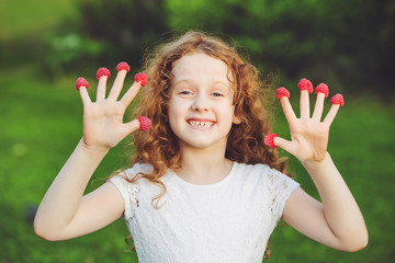 Little girl teasing is putting fingers to nose with raspberry. 