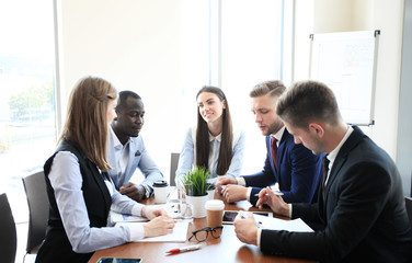 Young handsome woman gesturing and discussing something while his coworkers listening to him sitting at the office table