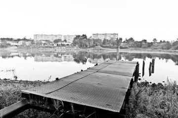 Metal pier on city river. Black and white image