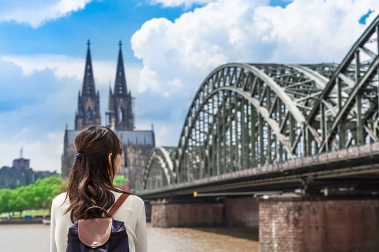 View to Cologne / Young woman seen from back looking to rhine river, huge bridge and famous cathedral of Cologne, Germany