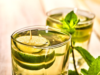 Alcohol drink. On wooden boards are top of two glasses with alcohol green transparent drink. A drink hundred fifty two mojito cocktail with lime and mint leaf . Country life still. Light background.
