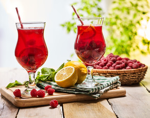 On wooden boards are ice cold beverage two glasses with red raspberry lemon cocktail . Alcohol country cocktail beverage number hundred seventy one with leaf mint. Outdoor country cocktail .