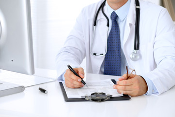 Close up of male doctor is sitting at the table and filling up medical history form