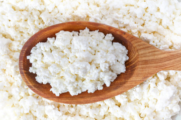 crumbly cottage cheese in the wooden spoon lying on the cottage cheese - 115854495
