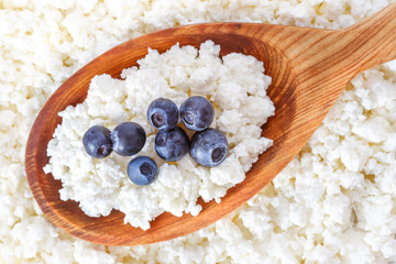 crumbly cottage cheese in the wooden spoon with blueberries on the top - 115854857