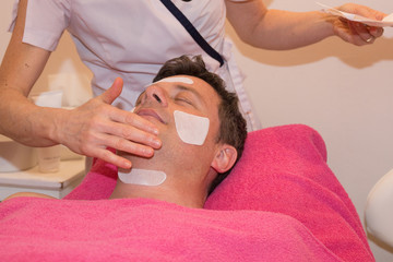 Hands of cosmetologist apply cream on man's face, closed eyes.