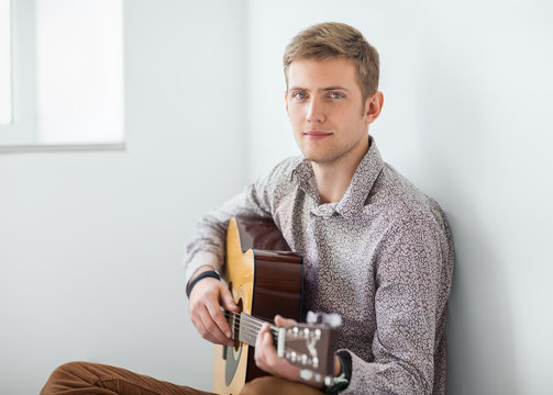 Portrait of handsome man playing guitar siting on floor