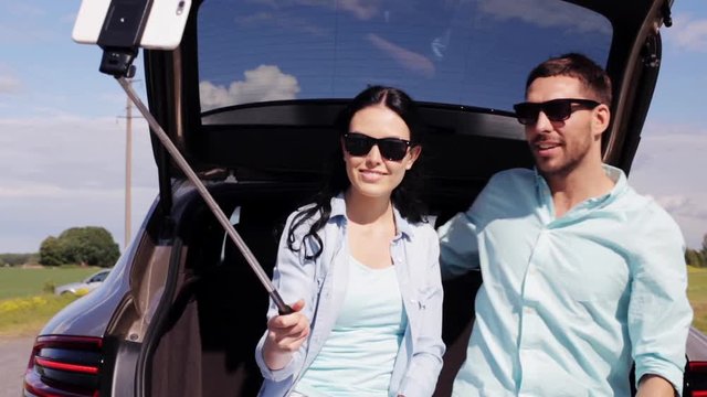 couple with smartphone selfie stick at car trunk 42
