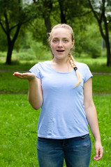 Portrait of happy surprised young pretty girl, showing something or blank copyspace area for slogan or text message, against green summer park background