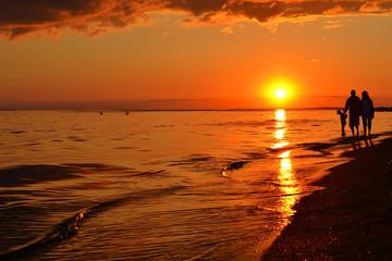 Obraz premium The family with the child walks on the seashore at sunset.