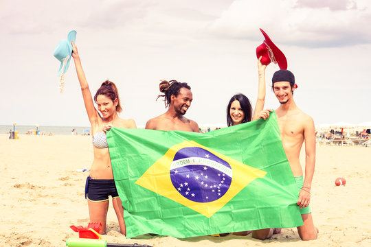 Group of cheerful friends holding brazilian flag at beach games party - Multiracial students having fun taking holiday photo on sand - Concept of joyful moment around the world