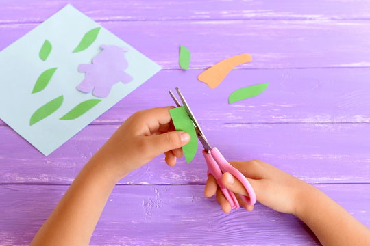 Child cuts a leaf from green paper. Kid holds scissors in his hands. Details to create a card. Child doing crafts from colored paper. Art project for kindergarten, summer camps