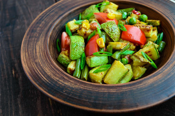 Dietary vegetarian salad with grilled zucchini, fresh tomatoes, sweet corn and herbs in a clay bowl on dark wooden background.