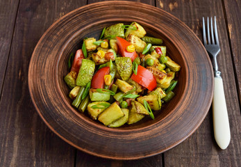 Dietary vegetarian salad with grilled zucchini, fresh tomatoes, sweet corn and herbs in a clay bowl on dark wooden background.