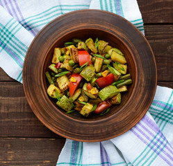 Dietary vegetarian salad with grilled zucchini, fresh tomatoes, sweet corn and herbs in a clay bowl on dark wooden background. The top view