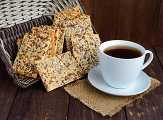 Dietary crunchy cracker with cereals (sunflower seeds, flax and sesame) and a cup of tea on a dark wooden background.