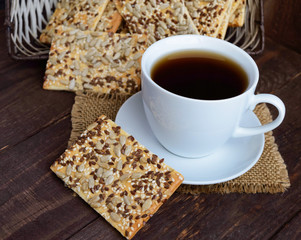 Dietary crunchy cracker with cereals (sunflower seeds, flax and sesame) and a cup of tea on a dark wooden background.