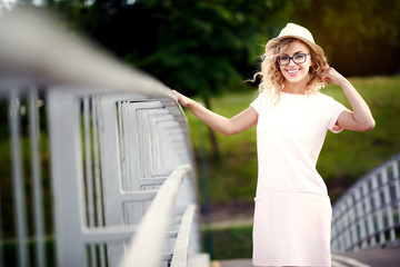 Young and beautiful cheerful girl in a hat and glasses walking in summer city and smiles