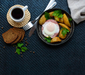 Fried egg in salami and baked potatoes. Submission of a frying pan with a cup of coffee and rye bread. Breakfast. The top view
