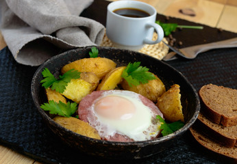 Fried egg in salami and baked potatoes. Submission of a frying pan with a cup of coffee and rye bread. Breakfast.