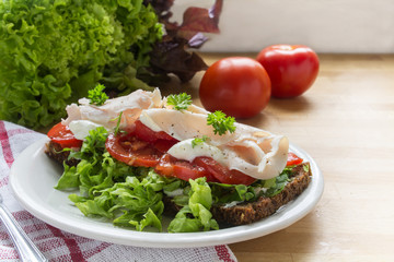 sandwich from dark wholemeal rye bread with tomatoes, green salad and chicken breast fillet on a kitchen board