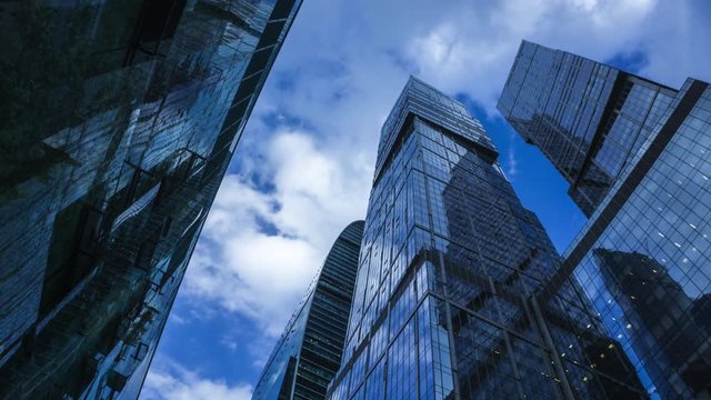 Modern reflective skyscrapers against cloudy sky 4K time lapse. View from below