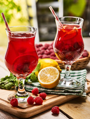 On wooden boards are ice cold beverage couple glasses with red raspberry lemon cocktail . Alcohol country cocktail beverage number hundred eighty with checkered napkin. Outdoor country cocktail .