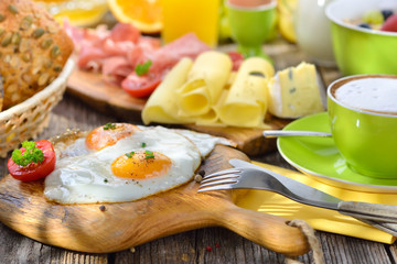 Gedeckter, rustikaler Frühstückstisch im Sonnenlicht mit Spiegeleiern und weiterer reichlicher  Auswahl - Outside served breakfast with with fried eggs a wide selection of other foods 