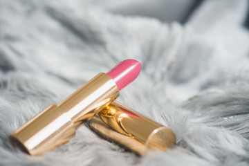 Pink lipstick in gold packaging. Grey,luxurious fur as background. 