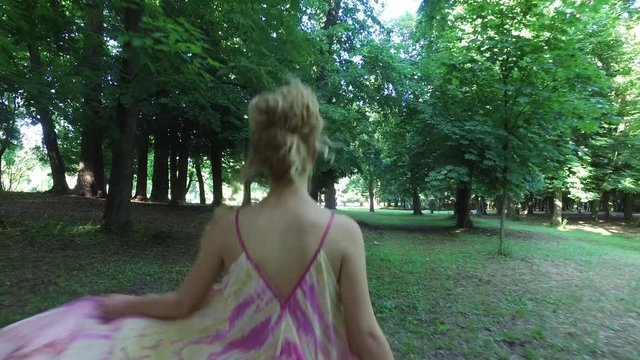Back view of blonde hair woman walking in a city park &ndash; airy, dreamlike concept