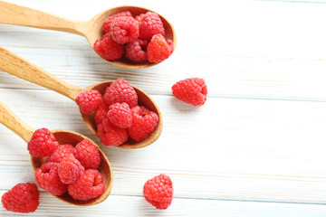 Red raspberries in spoon on a white wooden table