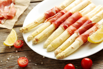 Fresh white asparagus wrapped in jamon on a grey wooden table