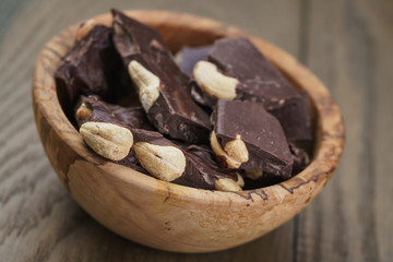 broken homemade bar of chocolate with cashew nuts in wood bowl