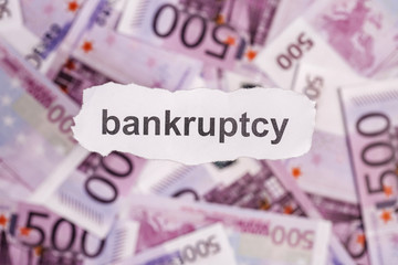 Focus on the word BANKRUPTCY on piece of torn white paper with banknote