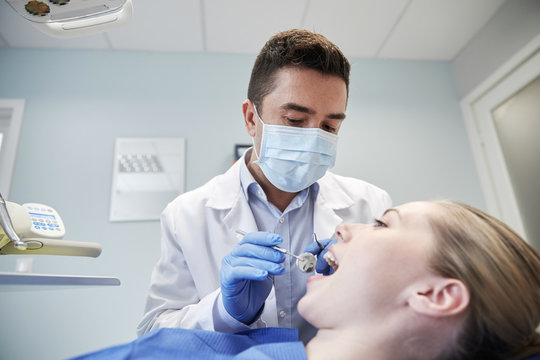 male dentist in mask checking female patient teeth