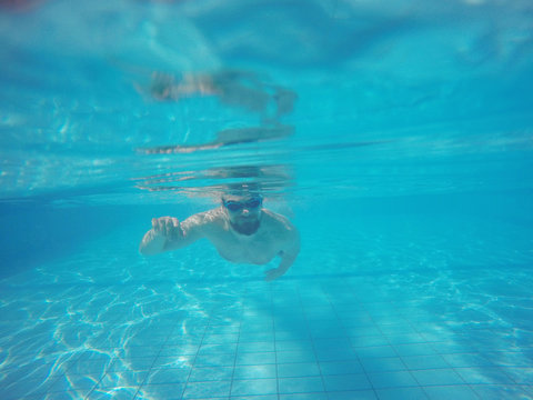 Beard man with glasses swimming under water in the pool