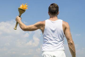 Torchbearer athlete in old fashioned white uniform holding sport torch against sunny blue sky