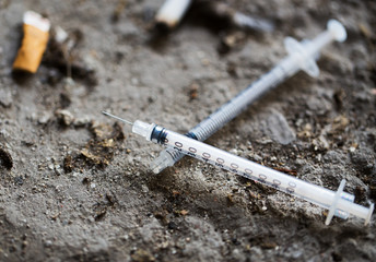 close up of syringe and smoked cigarette on ground