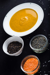 Cream soup of assorted lentil. Yellow and green lens, spices as raw for meal and lemon on black background. Healthy, appetizing, delicious, vegetarian food. Top view, copy space.
